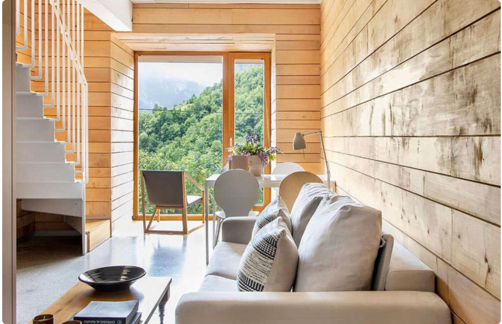 Salón de madera con escalera y ventanal al valle